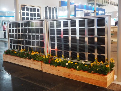 Drei Solarpanels mit bunten Blumen in einem Holzgefäß davor.